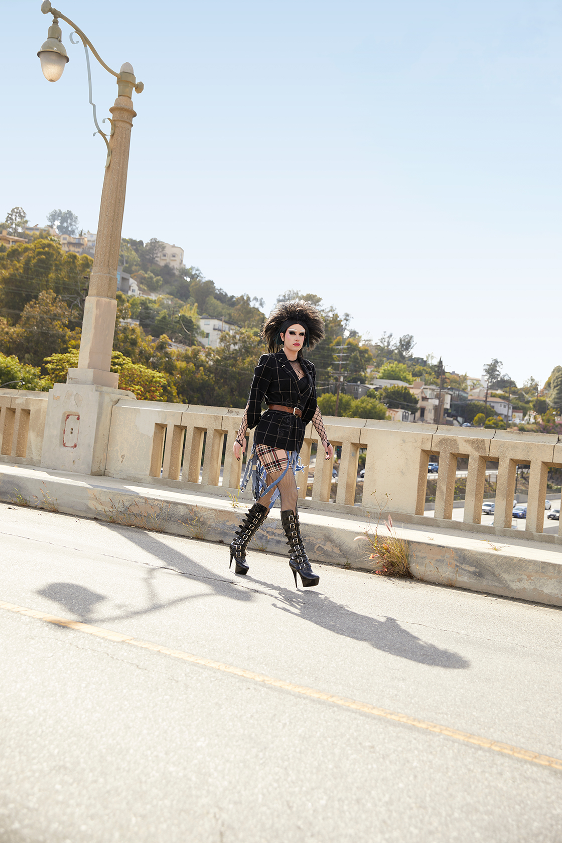 Full body image of Jesse in Punk inspired drag on a highway overpass walking forward and looking sideways toward the camera